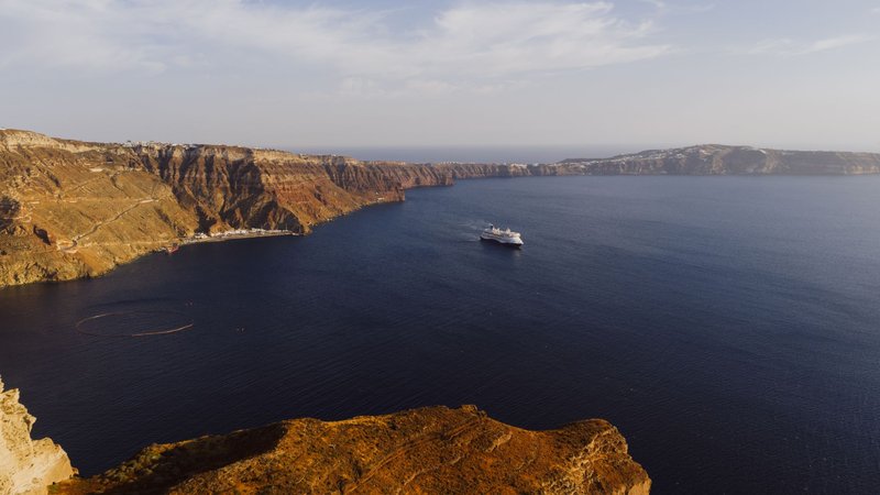 A breathtaking view of Fira, Santorini's caldera with a cruise ship sailing by the cliffs.