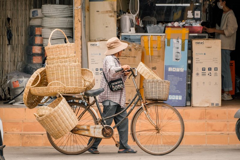 A woman pushes a bicycle carrying wicker baskets in Siem Reap, Cambodia, showcasing local market life.
