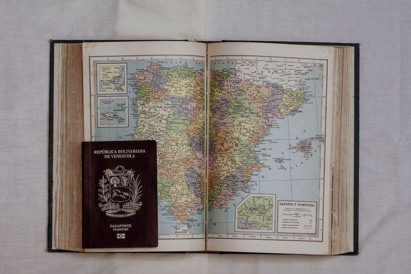 Open vintage atlas showing Spain and Portugal with a Venezuelan passport on top, symbolizing travel.