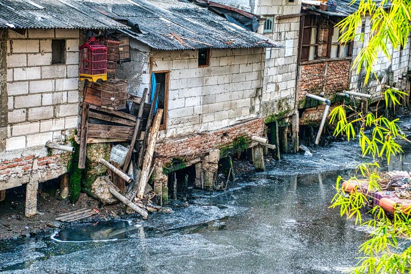 Polluted river beside rundown houses in Jakarta's slum, illustrating urban poverty and environmental issues.