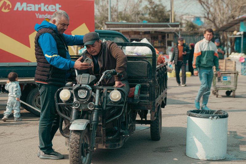 Local men interact at a bustling Uzbekistan marketplace with a motorbike cart.