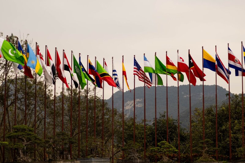 A display of various national flags on flagpoles set against a mountain backdrop, symbolizing global unity.