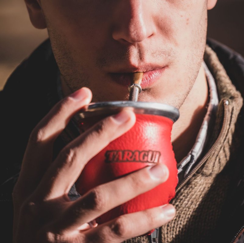 Close-up of a man drinking yerba mate with a straw from a red gourd.
