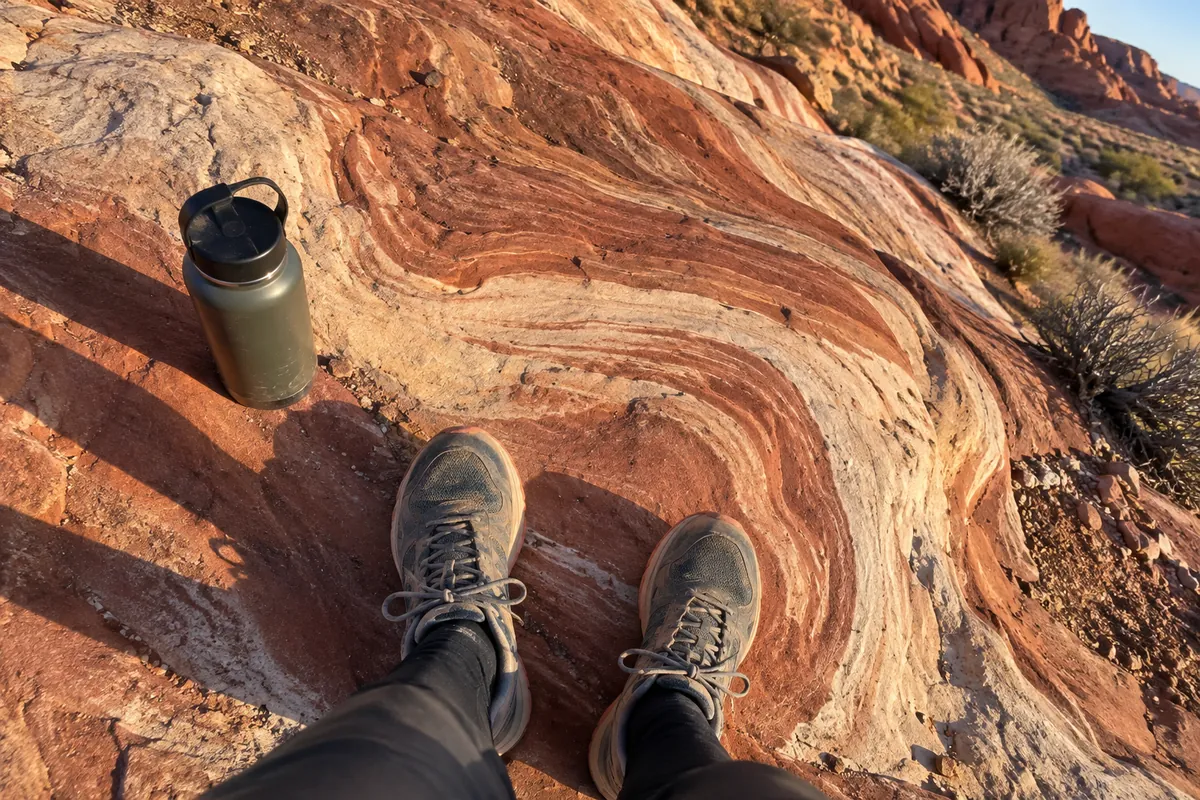 Feet in trail running shoes on red sandstone at Valley of Fire with a steel water bottle beside them
